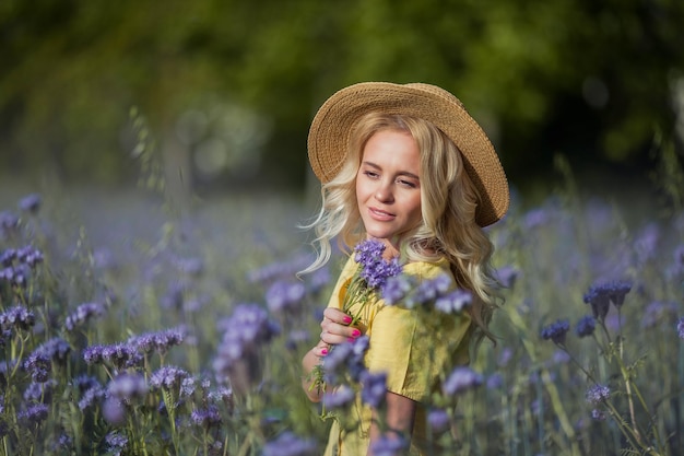 Rubia joven hermosa mujer con un sombrero camina por un campo de flores de color púrpura. El verano. Primavera.