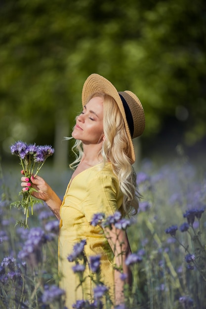 Rubia joven hermosa mujer con un sombrero camina por un campo de flores de color púrpura. El verano. Primavera.