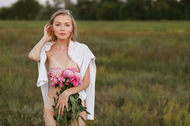 Rubia en lencería tiene flores rosas en sus manos