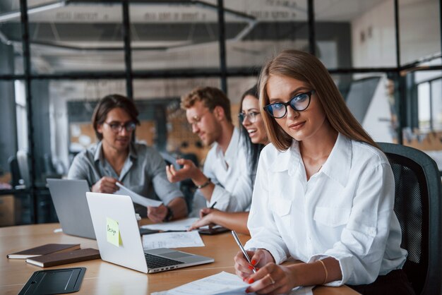 Rubia mira a la cámara. Jóvenes empresarios en ropa formal que trabajan en la oficina.