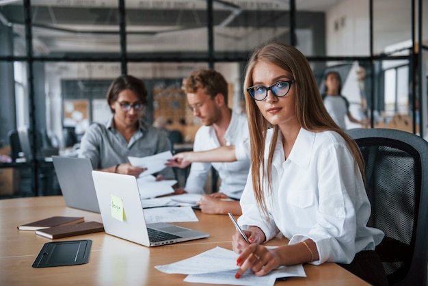 Rubia mira a la cámara. Jóvenes empresarios en ropa formal que trabajan en la oficina.