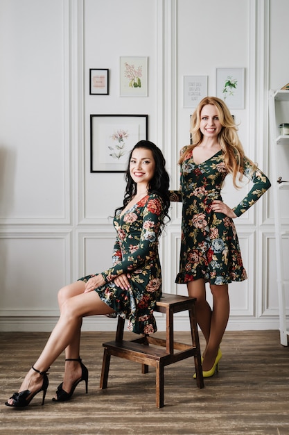 Rubia y morena con vestidos cortos y verdes con estampados. Dos chicas guapas en un estudio blanco.