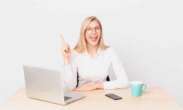 Rubia mujer bonita joven mujer rubia que se siente como un genio feliz y emocionado después de darse cuenta de una idea y trabajar con una computadora portátil