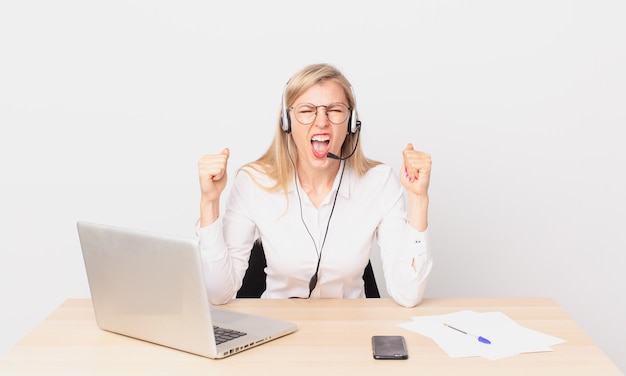 Rubia mujer bonita joven rubia gritando agresivamente con una expresión de enojo y trabajando con una computadora portátil