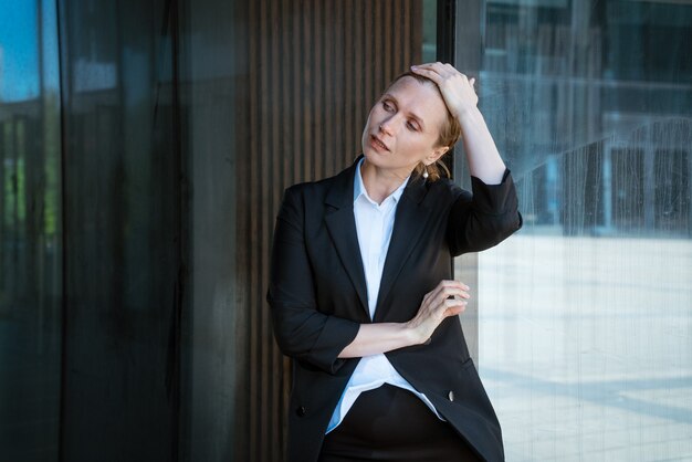 Foto rubia de mujer de negocios en un traje alisa su cabello cerca del edificio de oficinas