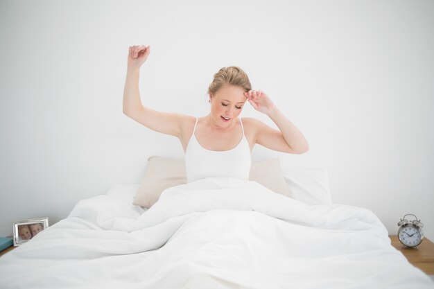 Rubia natural bostezando sentado en la cama con los ojos cerrados