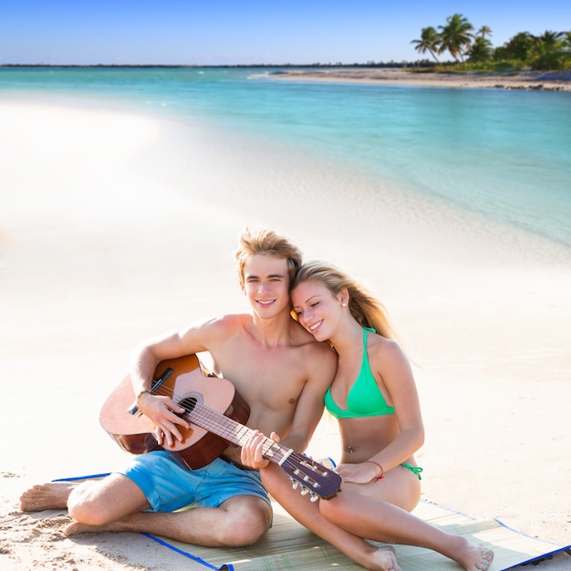 Rubia pareja de turistas tocando la guitarra en la playa