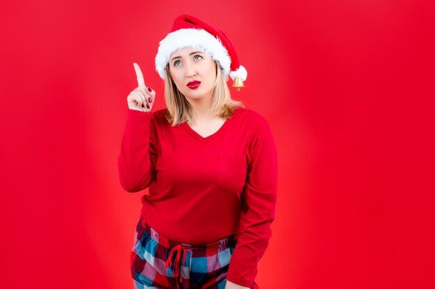 Rubia en pijama de Navidad sobre un fondo rojo muestra gestos con sus dedos índices