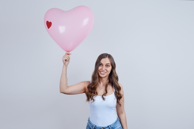 Rubia sonriente con rizos sosteniendo un globo rosa en forma de corazón. Feliz día de San Valentín.