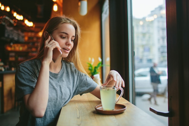 La rubia usa el teléfono. Chica y smartphone. Una mujer está sentada en un café con un celular.