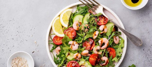 Rucola-, Gurken-, Tomaten- und Garnelensalat mit Sojasauce auf einer Keramikplatte. Selektiver Fokus. Ansicht von oben.