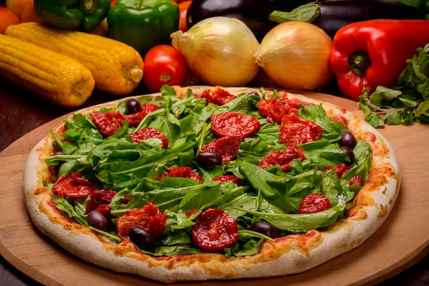 Rucola und sonnengetrocknete Tomatenpizza auf Holzbrett und Gemüse im Hintergrund.