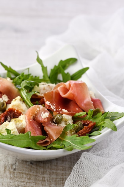 Rucolasalat, Prosciutto mit sonnengetrockneten Tomaten, Mozzarellascheiben, Kapern, abgeschmeckt mit Olivenbutter und Parmesan. Ein Gericht für diejenigen, die ihre Gesundheit überwachen