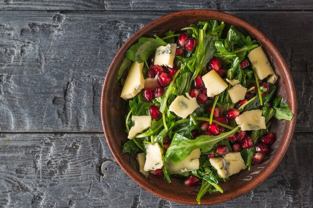 Rúcula con granada y queso con moho azul en un plato sobre una mesa de madera. Ensalada vegetariana dietética. Endecha plana.