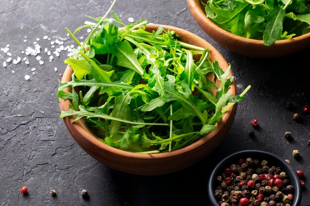 Rúcula orgánica fresca para ensalada en cuenco de madera sobre fondo negro de cerca. Vista superior.