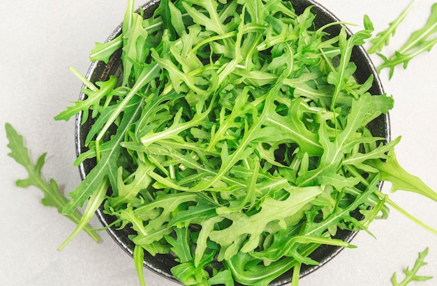 Rúcula verde fresca em tigela de cerâmica na mesa de cozinha cinza vista superior do espaço de cópia Erva picante de primavera para alimentação saudável