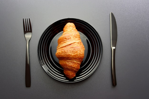 Ruddy croissant sobre una placa negra con un tenedor y un cuchillo sobre un fondo gris