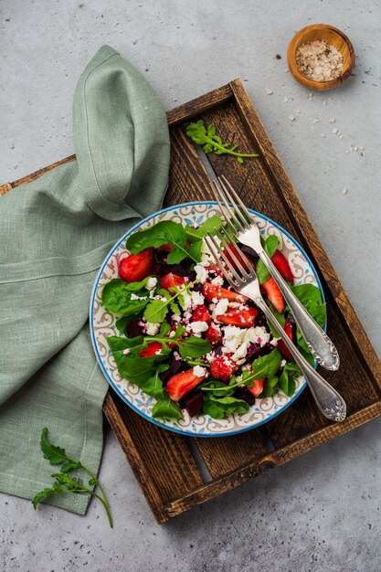 Rüben, Erdbeeren, Feta-Käse und Rucola-Salat in Keramikplatte auf alten Betontischoberfläche. Draufsicht.