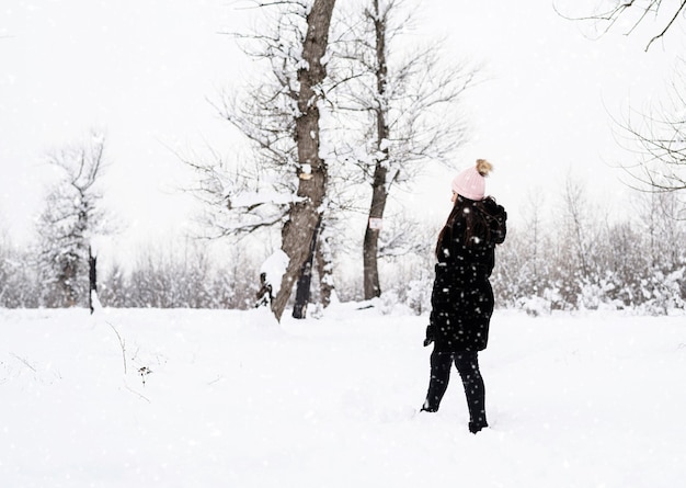 Rückansicht der brünetten Frau, die im verschneiten Park im Schneefall geht