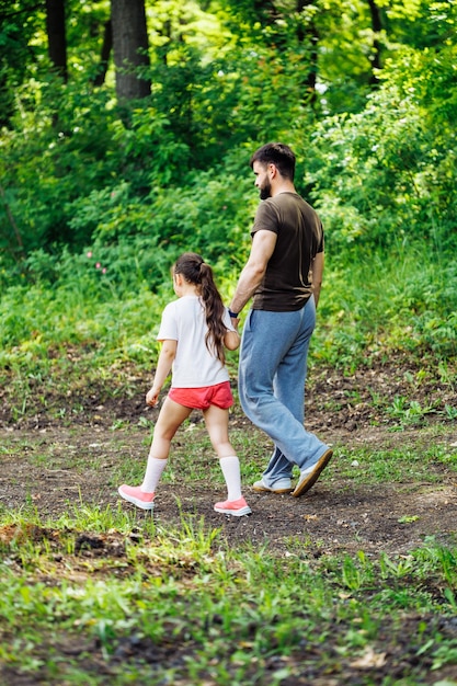 Rückansicht der Familie, die im Parkwald um Bäume spazieren geht und Spaß hat Sommeraktivitäten, die vertikal reisen