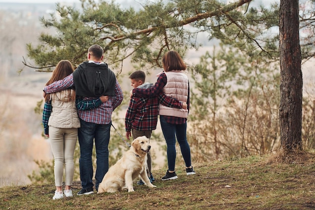 Rückansicht der Familie, die zusammen mit ihrem Hund draußen im Wald steht