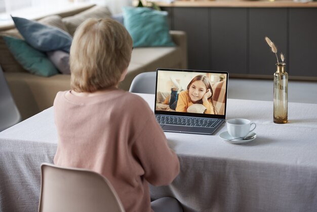 Rückansicht der Großmutter, die während der Sperrung online auf einem Laptop mit ihrer Enkelin spricht