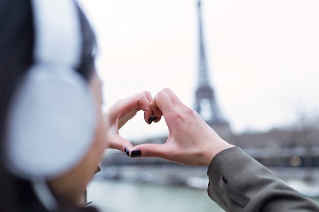 Rückansicht der jungen Frau, die das Herzsymbol mit seinen Händen zum Eiffelturm von der Seine in Paris, Frankreich, macht.