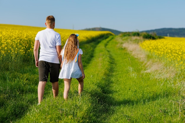 Rückansicht der Kinder Bruder und Schwester, die weit weg auf einem Weg mit Gras gehen, umgeben von gelben Feldern gegen den Himmel