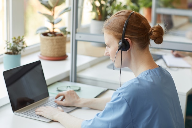 Rückansicht der Kundendienstmitarbeiterin des Kunden, die an ihrem Arbeitsplatz sitzt und am Laptop im Büro arbeitet