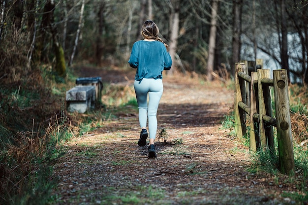 Rückansicht der nicht erkennbaren passenden Frau in Aktivkleidung, die entlang Spur im grünen Wald läuft