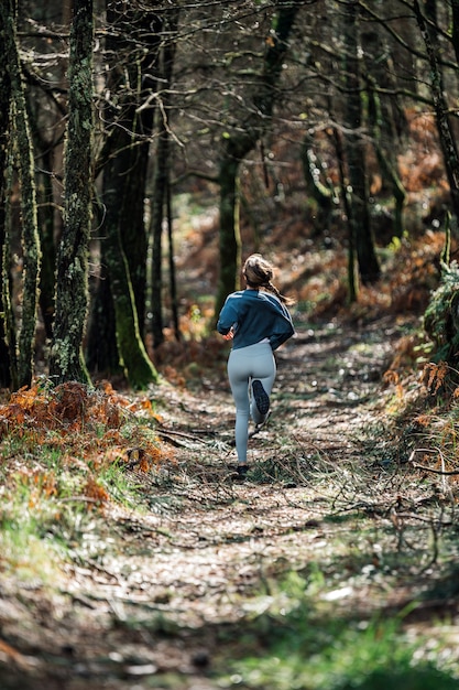 Rückansicht der nicht erkennbaren passenden Frau in Aktivkleidung, die entlang Spur im grünen Wald läuft