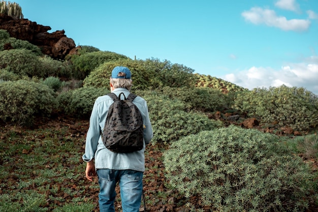 Rückansicht des alten Senioren, der einen gesunden Lebensstil genießt, geht Trekking in Bergumgebung Älterer kaukasischer Mann mit Hut und Rucksack, der mit Sportstock geht