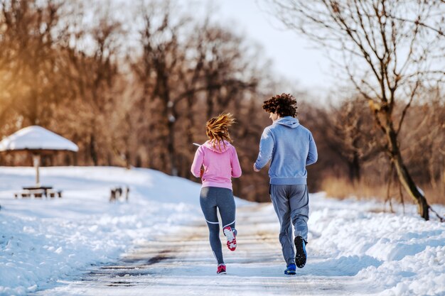 Rückansicht des engagierten hübschen kaukasischen Paares, das in der Natur läuft. Winter. Outdoor-Fitness-Konzept.