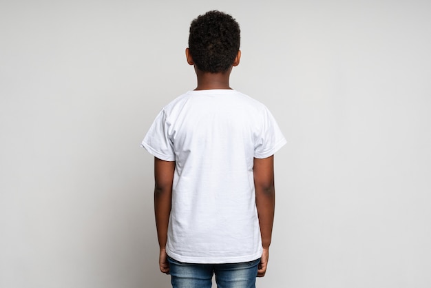 Rückansicht des gemischtrassigen Jungen, der weißes T-Shirt trägt. Konzept der Kindheit. Isoliert auf weißem Hintergrund, Studioaufnahme