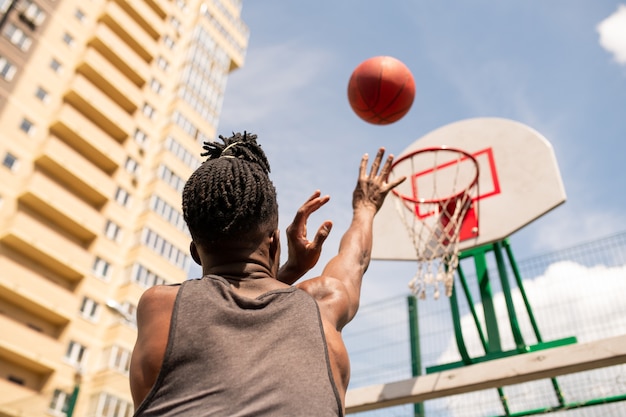 Rückansicht des jungen afrikanischen Basketballspielers, der Ball im Korb beim Training in der städtischen Umgebung wirft