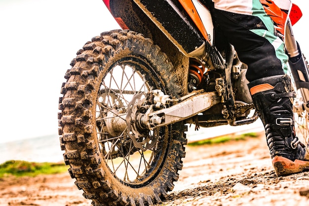 Rückansicht des jungen Mannes, der in die Ferne blickt und bei Sonnenuntergang auf dem Motorrad am Strand sitzt