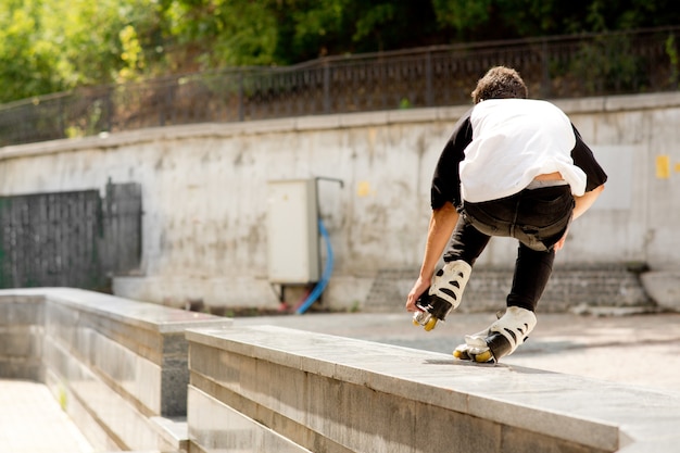 Rückansicht des jungen professionellen Skaters, der Stunts außerhalb macht. Städtische moderne Ansicht. Skaten auf einem Bein. Tageslicht draußen.