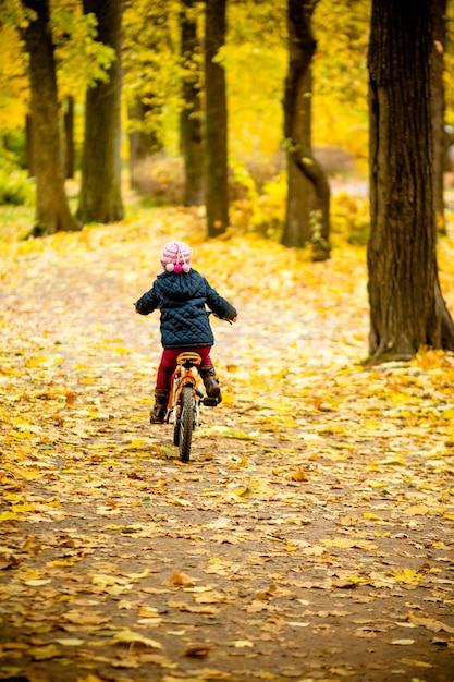 Rückansicht des kleinen Kindes im blauen Mantel, der ein Fahrrad reitet.