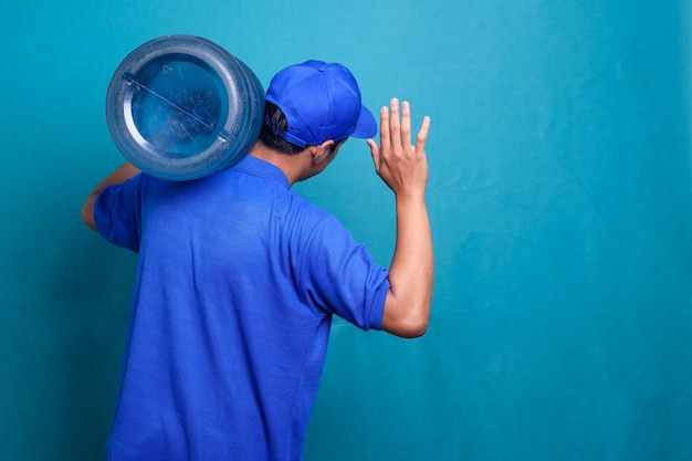 Rückansicht des Lieferanten in blauer Uniform, der als Händlerkurier mit einer Wassergallone arbeitet