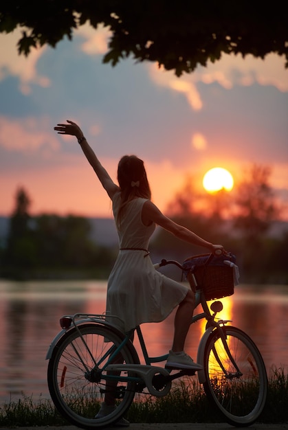 Rückansicht des Mädchens mit Retro-Fahrrad, auf dem der Korb bei Sonnenuntergang die feurige Sonne genießt