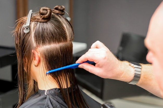Rückansicht des männlichen Friseurs, der nasses Haar der jungen kaukasischen Frau kämmt, teilt sich in Abschnitte in einem Friseursalon