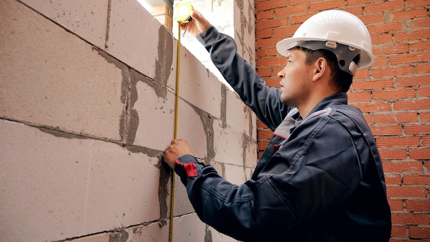 Rückansicht des Mannes, der vor Ort arbeitet und das Fenster in der Mauer mit Lineal misst