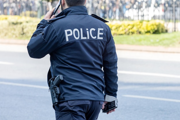 Rückansicht des Polizisten mit Smartphone auf der Straße der Stadt