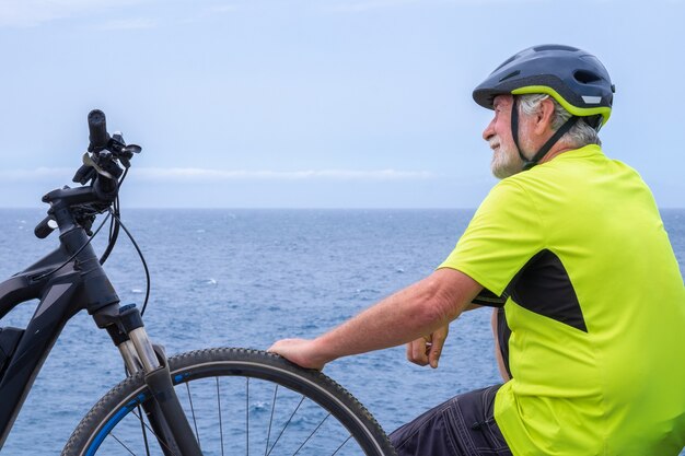 Rückansicht des Radfahrers, der nach der Aktivität mit dem Elektrofahrrad auf der Klippe auf dem Meer ruht