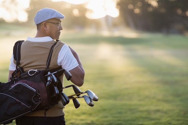 Rückansicht des reifen Mannes, der Golftasche trägt