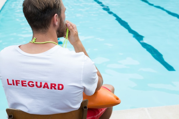 Rückansicht des Rettungsschwimmers, der auf Stuhl sitzt und am Pool pfeift