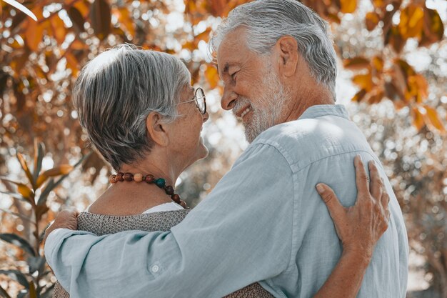 Rückansicht des schönen weißhaarigen Seniorenpaares, das sich beim Spaziergang im Wald umarmt Lächelnde ältere Großeltern genießen einen ruhigen Ruhestand und schauen sich gegenseitig in die Augen