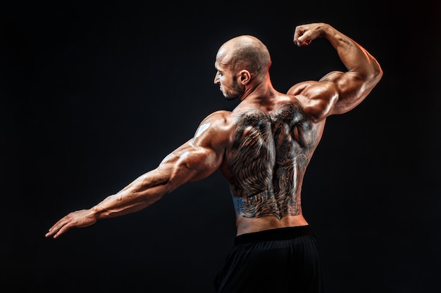 Rückansicht des tätowierten Bodybuilders mit ausgestreckten Armen