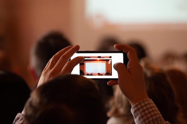 Rückansicht des Teilnehmers im Publikum, der mit dem Smartphone ein Foto der Präsentation macht