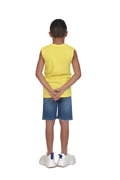 Rückansicht des vollständigen Porträts eines Jungen in kurzen Hosen und ärmellos mit Händen auf dem Rücken auf weißem Hintergrund